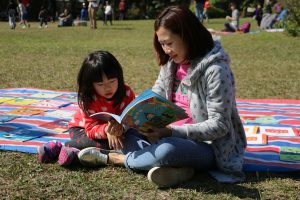A parent and child reading together at a picture books and music festival.